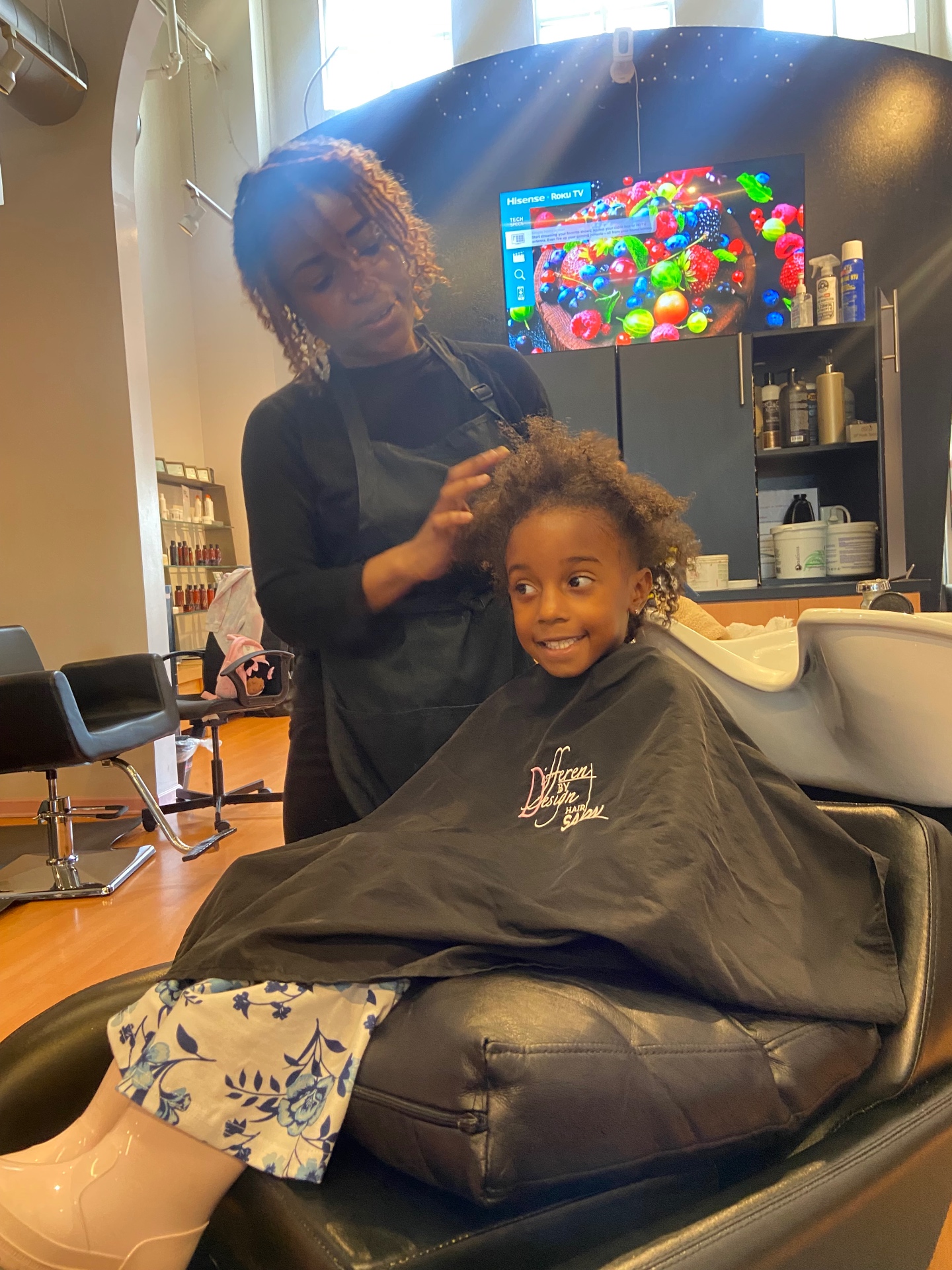 Valerie gently examining a young client's natural hair in the salon